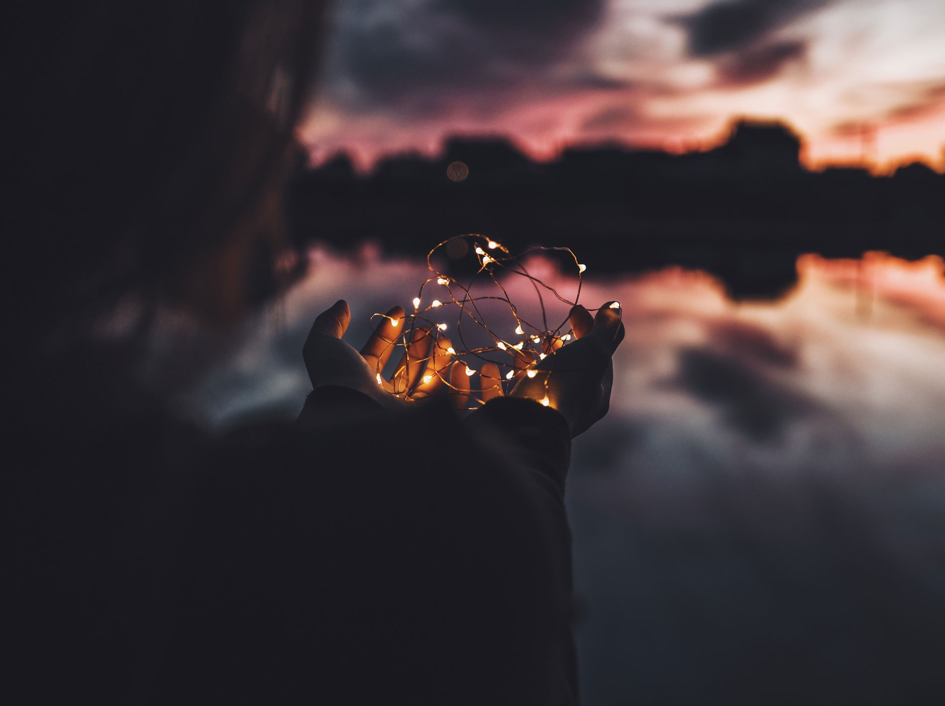 Mains tenant une guirlande de lumière au crépuscule, évocation d’un temps de calme pour soi